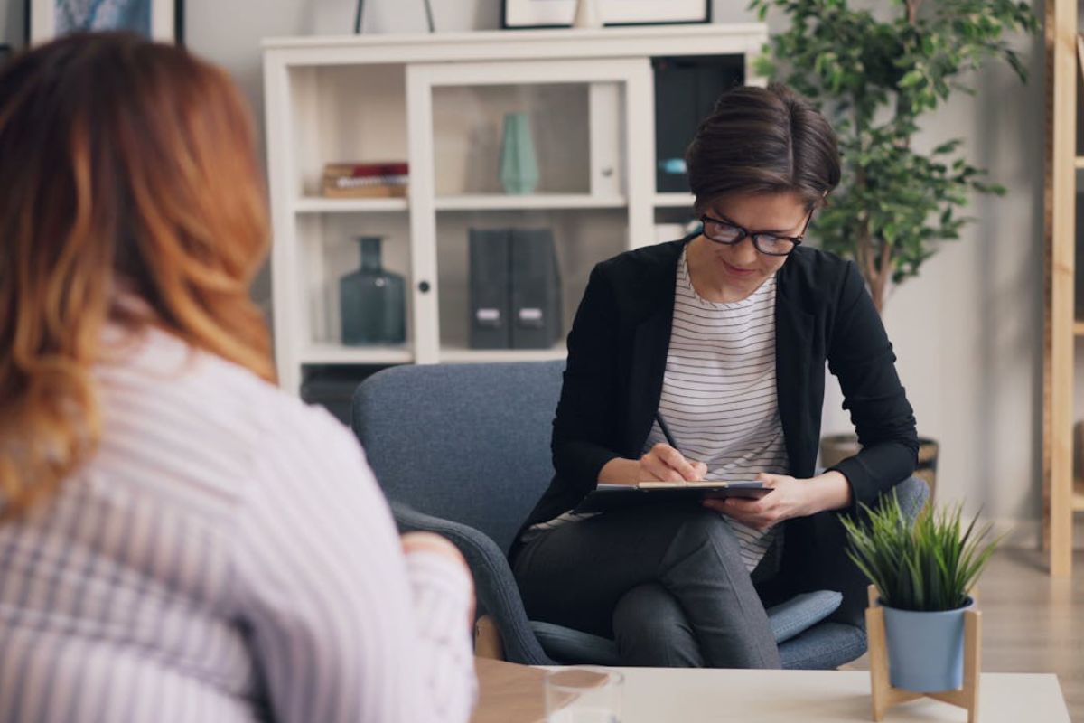 a therapist taking notes during a court-ordered therapy session with a female client in a modern office