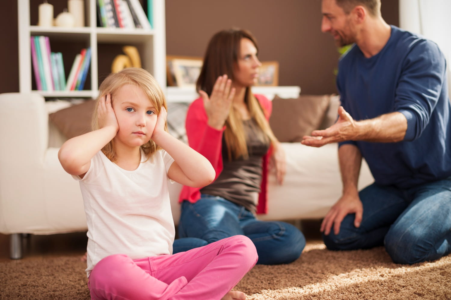 A child covering her ears because her parents are quarreling